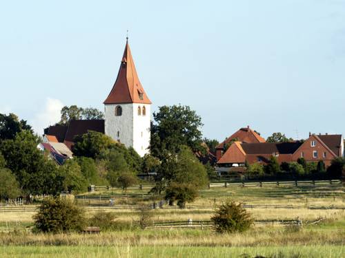 Landschaft mit Dorf und Kirchturm im Hintergrund.