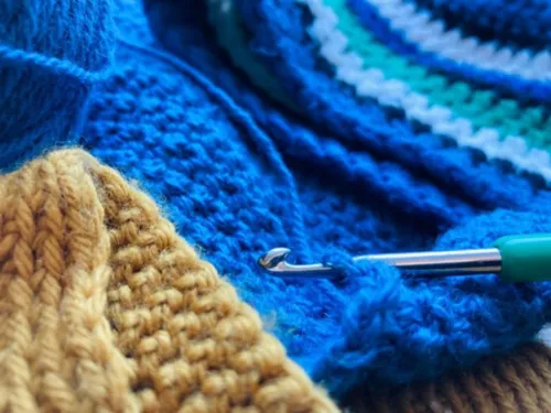 Häkelnadel liegt auf einem blauen gehäkelten Schal mit Mustern.