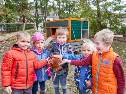 Fünf Kita Kinder, die ein Huhn halten, im Hintergrund ein Hühnermobil