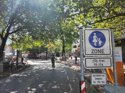 Eine Straße mit Radfahrer und Bäumen, rechts ein Schild Fußgängerzone