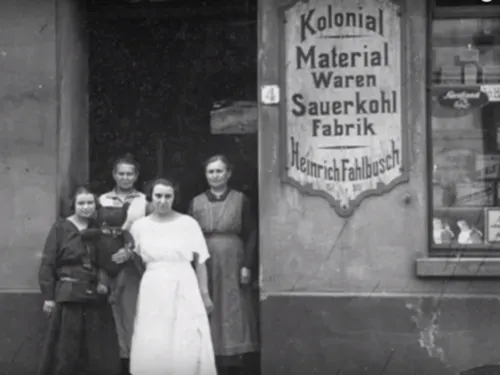 Ein altes Schwarz-Weiß-Foto: Vier Frauen in einem Hauseingang neben dem Schild "Kolonial Material Waren Sauerkohl Fabrik Heinrich Fahlbusch.