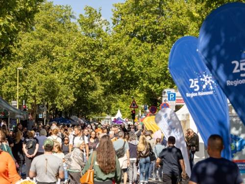 Auf einer langen Straße gehen viele Menschen bei Sonnenschein.