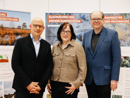 Drei Personen vor Plakatwänden