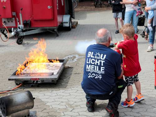 Ein Mann unterstützt einen kleinen Jungen, der mit einem Feuerlöscher ein Feuer löscht.