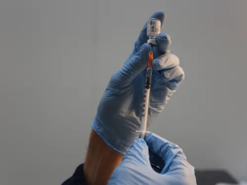 Hände in blauen Handschuhen ziehen ein Impfdosis in eine Spritze