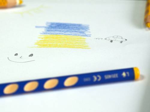 Einfache Zeichnung mit Buntstiften auf einem weißen Blatt Papier: Die Farben Blau und Gelb, eine Sonne, ein grinsendes Gesicht und ein Auto. Auf dem Blatt verteilt liegen Buntstifte.