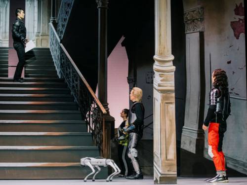 Drei Personen und ein Roboter schauen zu einer vierten Person auf einer Treppe hinauf.