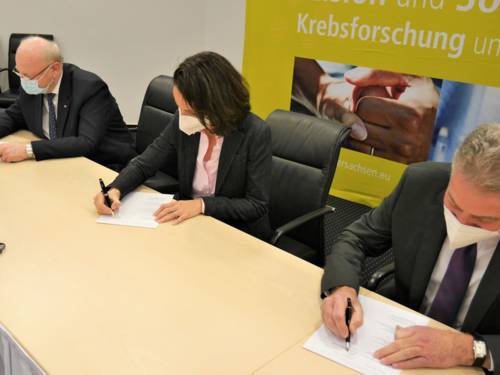 Eine Frau und zwei Männer mit Nasen-Mundschutz-Masken unterschreiben etwas.