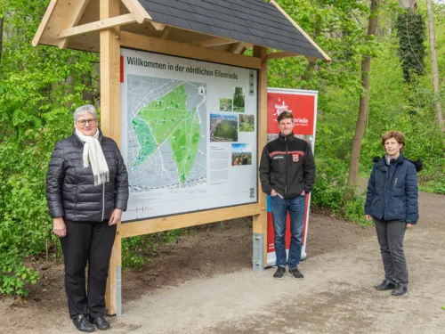 Drei Personen stehen an einem Waldeingangsschild