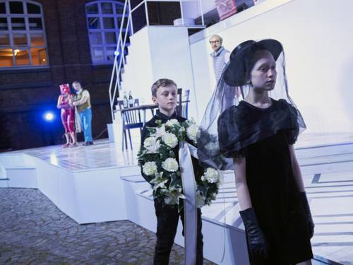 Ein Frau in Trauerkleidung gefolgt von einem Jungen mit einem Trauerkranz.