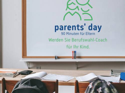 Tafel mit der Aufschrift "parent's day, 90 Minuten für Eltern. Werden Sie Berufswahl-Coach für Ihr Kind" in einem Klassenzimmer.