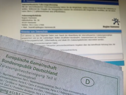 Fahrzeugbrief vor einer Anmeldemaske auf einem Bildschirm