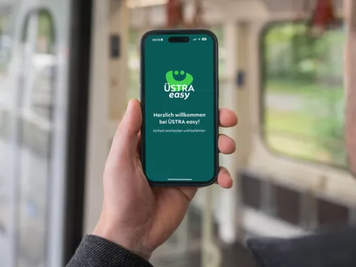 Eine Hand hält ein Smartphone in der Hand und hat die App namens Üstra easy auf dem Display angezeigt