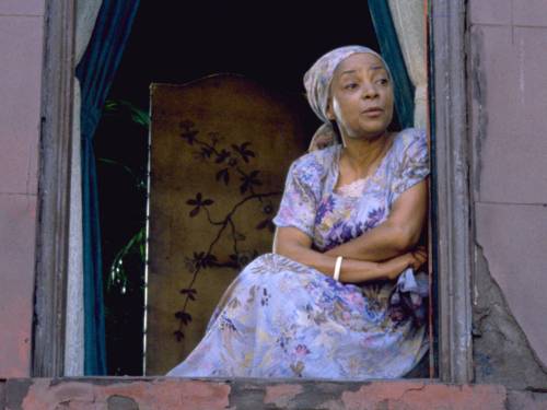 Eine Frau sitzt auf der Fensterbank eines geöffneten Fensters und schaut hinaus.