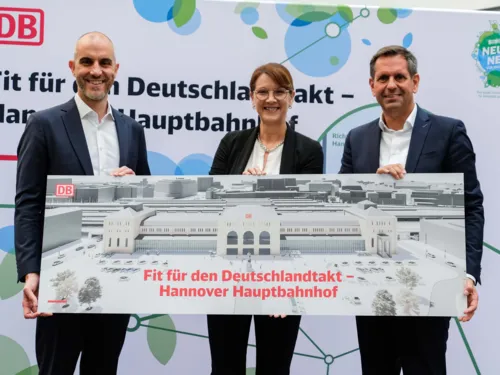 Drei Personen, die ein Schild halten. Darauf steht "Fit f&uuml;r den Deutschlandtakt &ndash; Hannover Hauptbahnhof".