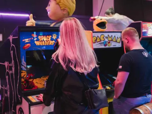Eine Frau und ein Mann spielen jeweils an einem Videospielautomat