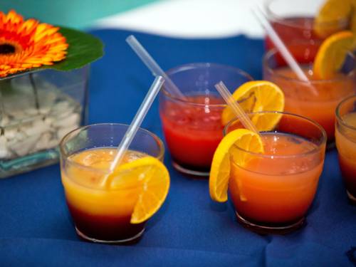 Fruchtsäfte sind in verschiedenen Trinkgläsern zu Cocktails in wechselnden Rot- und Orangetönen gemixt.