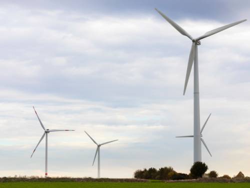 Vier Windkraftanlagen stehen auf einer freien Fläche.