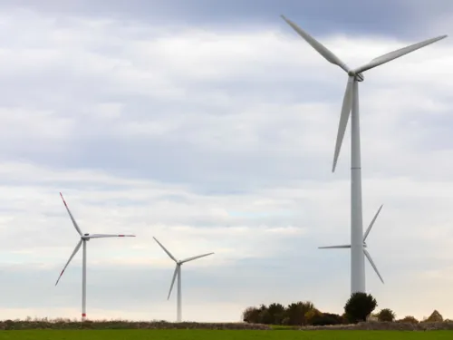 Vier Windkraftanlagen stehen auf einer freien Fläche.