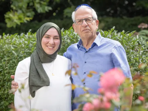Zwei Personen stehen in einem Garten und legen sich jeweils einen Arm um die Schulter.