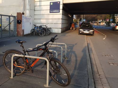 Ein Fußweg, rechts eine Straße mit einer Unterführung. Auf dem Fußweg befinden sich vorne vier Fahrradbügel, ein Rad ist angeschlossen, hinten links stehen weitere Räder an Fahrradbügeln vür einer Wand, an der ein blaues Schild hängt, auf dem Ledeburg zu lesen ist.