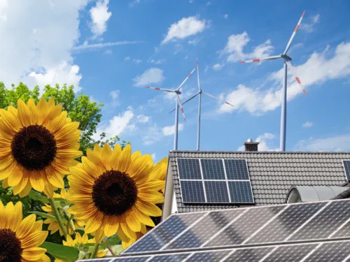 Sonnenblumen, Solarmodule und Windräder vor einem wolkigen Himmel.