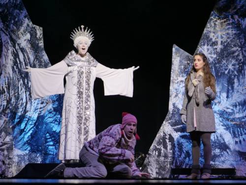 Zu sehen ist eine Bühnenaufnahme des Musicals "Die Schneekönigin": Die Schneekönigin in einem weißen Outfit singt, Kay und Gerda befinden sich auch auf der Bühne.
