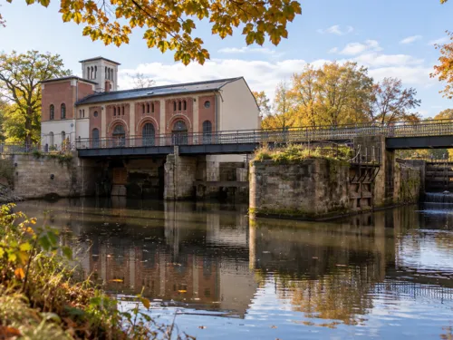 Blick auf die Historische Wasserkunst Hannover. Davor ein Kanal und darüber eine Brücke.