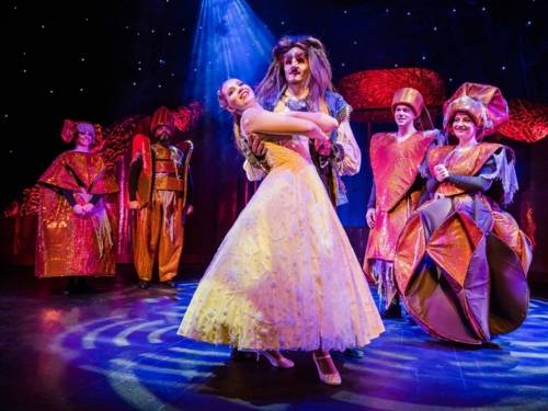 Zu sehen ist ein Bühnenbild des Musicals „Die Schöne und das Biest“: Belle und das Biest stehen in der Mitte, vier weitere Menschen sind um sie herum verteilt.