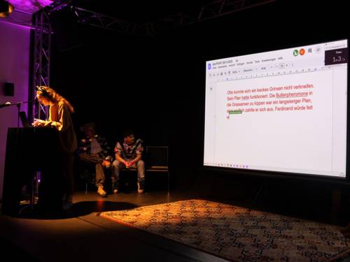 Eine Frau schreibt an einem Dokument, das öffentlich auf einer Leinwand abgebildet wird.