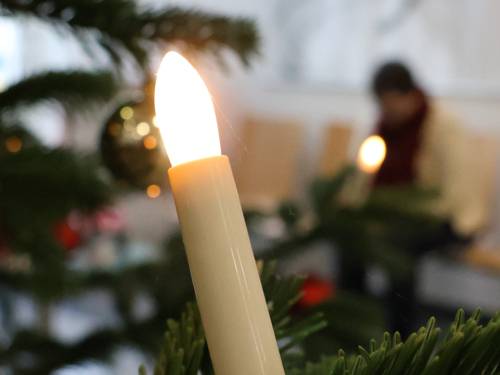 Eine Kerze an einem Weihnachtsbaum mit einer deprimiert wirkenden Person im Hintergrund