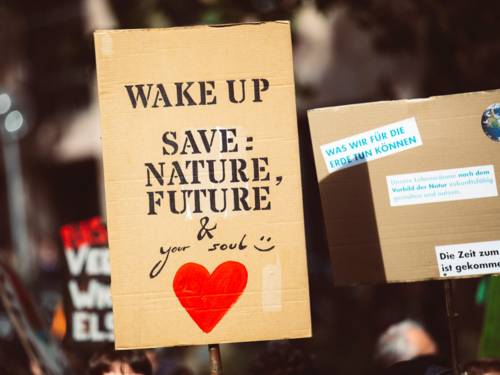 Ein Pappschild wird in die Höhe gehalten. Darauf steht: Wake up! Save: Nature, future and your soul.