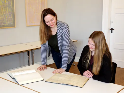 Zwei Frauen sichten historische B&uuml;cher an einem Tisch.