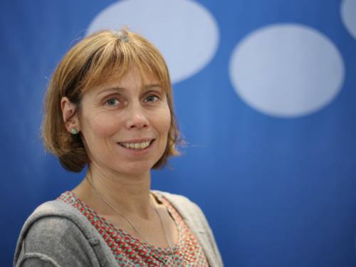 Porträtfoto von Sylvia Thiel vor einem blauen Hintergrund.