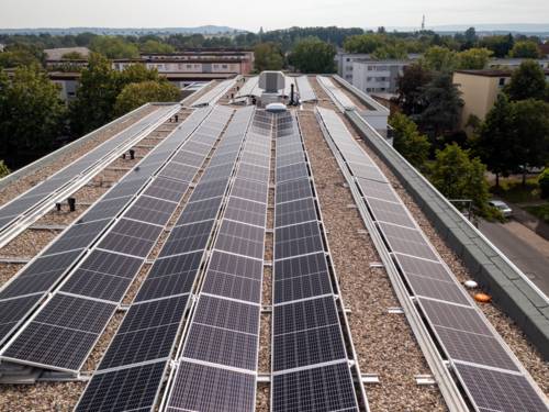 Auf einem modernen Flachdach sind lange Reihen von Photovoltaikmodulen zur Stromerzeugung installiert, die Oberflächen der Solarmodule sind in unterschiedliche Richtungen ausgerichtet.