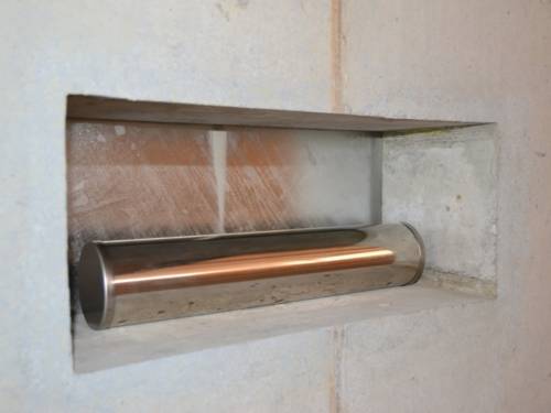 Eine kupferfarbene Metalröhre liegt in einer rechteckigen Maueröffnung.