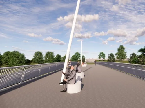 Auf einer breiten Brücke mit Fußweg sind in der Mitte zwei weiße Sitzelemente, darauf sitzt ein Mann im Anzug.