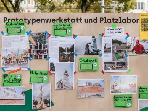 Auf einer Holzwand im Freien mit der Überschrift "Prototypenwerkstatt und Platzlabor" sind zahlreiche Bilder und Vorschläge zur Umgestaltung des Steintorplatzes befestigt.