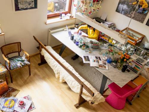 Blick von einer höher gelegenen Position auf den Arbeitsbereich in einem Atelier. Eine Künstlerin sitzt an einem großen Tisch und arbeitet.