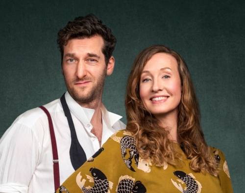 Ein Mann mit kurzem Haar, Bart und hochgezogenem Mundwinkel und eine lächelnde Frau mit langen Locken