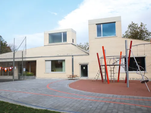 Ein leerer Spielplatz vor einem hellen Geb&auml;ude.