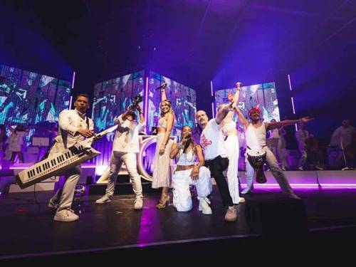 Drei Frauen und drei Männer stehen mit Mikrofonen oder Instrumenten in der Hand auf einer Bühne