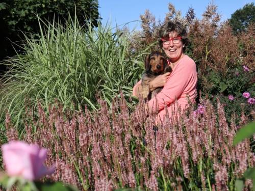 Zu sehen ist Katrin Iskam. Sie hält einen Hund in den Armen und befindet sich inmitten von Blumen.