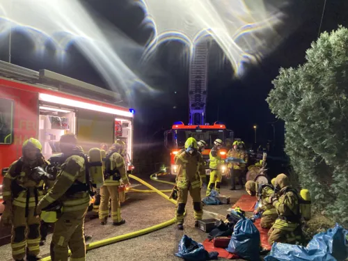 Viele Einsatzkräfte, die sich gerade einsatzbereit machen, im dunkeln, beleuchtet von zwei großen Feuerwehrautos.