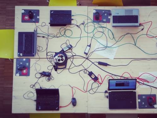 Ein großer Tisch, auf dem einige Laptops stehen, umringt von Kabelgewirr.