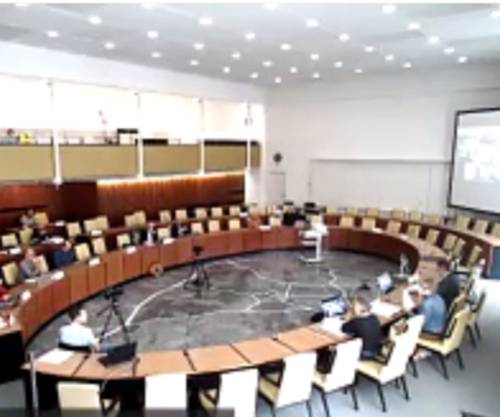 Screenshot aus einer Videokonferenz: Zu sehen ist der Ratssaal im Neuen Rathaus, im Plenum sitzen etwa zehn Personen. Auf einer Leinwand am rechten Rand des Bildes sind die Kacheln einer Videokonferenz zu sehen.