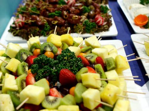 Spieße mit Obst, Käse und anderen Lebensmitteln liegen auf verschiedenen Tellern und Platten.