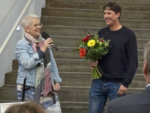 Frau mit Mikrofon und Mann mit Blumenstrauß auf einer Bühne