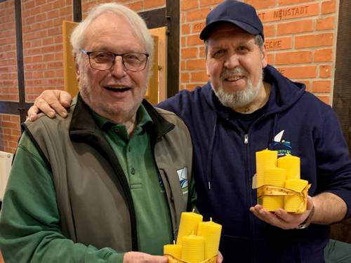 Zwei Männer halten jeweils Kerzen aus Bienenwachs in ihren Händen.