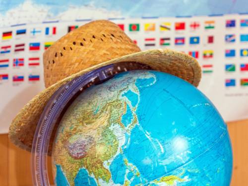 Ein Strohhut liegt auf einem Globus, dahinter ist eine Karte mit den Flaggen verschiedener Nationen an die Wand gepinnt.